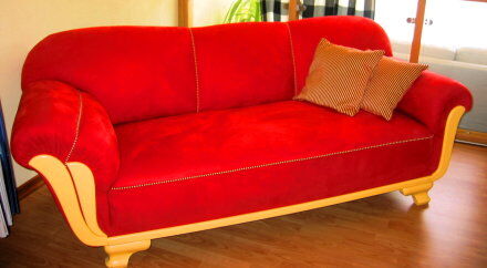 Rotes Sofa mit gelben Holzfüßen und gestreiften Kissen
